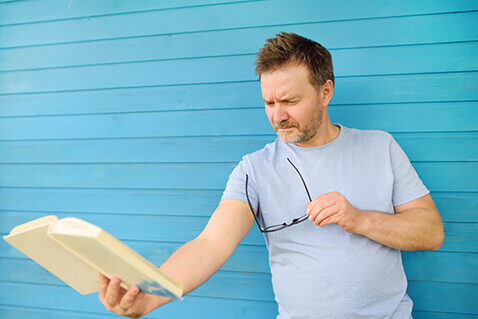 Man with presbyopia holding book at arm's length to read