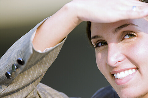 Smiling woman in suit blocking sun from her eyes with her hand